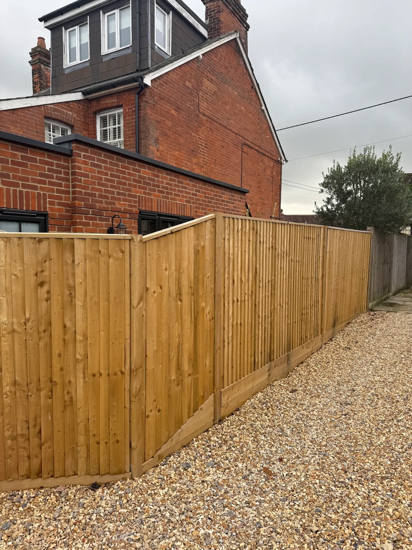 New close-board timber fence running along a gravel path beside a red-brick house